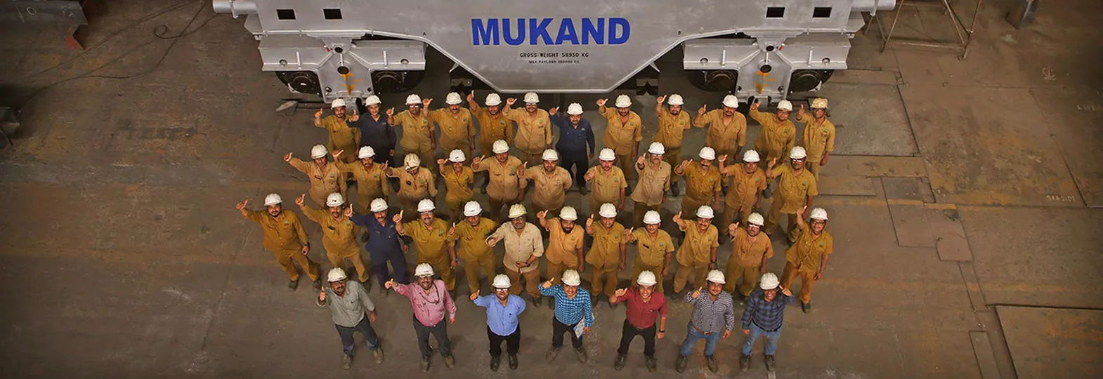 Group of industrial workers wearing safety helmets beneath a large overhead crane